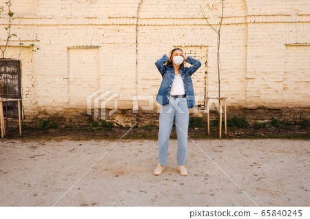 Adult woman in protective mask on street against exterior of old building 65840245