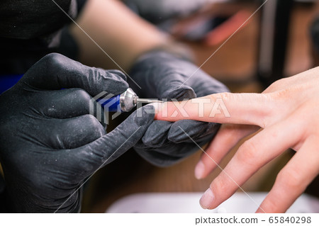 Manicurist use electric nail file drill in beauty salon. Perfect nails manicure process close up with burst flying debris. Manicurist use electric nail file drill in beauty salon. Perfect nails manicure process close up with burst flying debris. 65840298