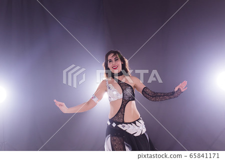 Young woman belly dancer in exotic dress with gold, dancing tribal fusion dance in studio. Young woman belly dancer in exotic dress with gold, dancing tribal fusion dance in studio. 65841171