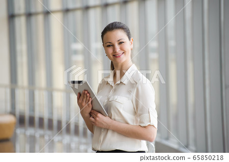 Young businesswoman talking on mobile phone while standing by window in office. Young businesswoman talking on mobile phone while standing by window in office. 65850218