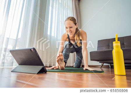 Fitness woman exercising on the floor at home and watching fitness videos in a tablet. People do 65850806