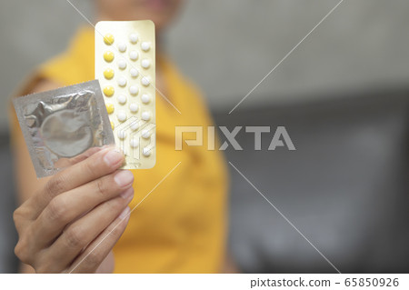 Woman hand holding contraceptive pills and condom sitting on sofa background. Woman hand holding contraceptive pills and condom sitting on sofa background. 65850926