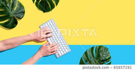 Person using a computer keyboard with tropical leaves 65857191