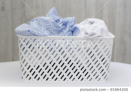 Blue and white dirty things in a white plastic laundry basket on a gray wall background. Washing, home cleaning Blue and white dirty things in a white plastic laundry basket on a gray wall background. Washing, home cleaning 65864208