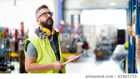 Technician or engineer with protective headphones standing in industrial factory. 65865758