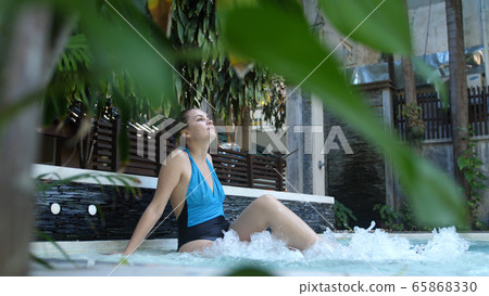 Beautiful young woman relaxes in a hydromassage jacuzzi, in swimming pool. Concept: spa procedures, body massages, spa cream, relax, spa water treatments 65868330