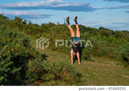 Young girl in a hat doing a handstand on the green hill. Young girl in a hat doing a handstand on the green hill. 65869291
