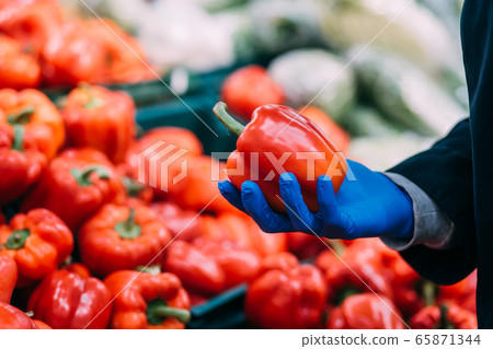 A man in gloves chooses red bell peppers in a grocery store, at the market. Hand take the pepper from a vegetable basket. A man in gloves chooses red bell peppers in a grocery store, at the market. Hand take the pepper from a vegetable basket. 65871344