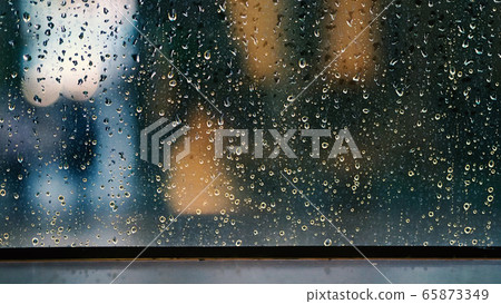 Window and rain drop in condominium or apartment room on a rainy day in Bangkok Thailand and background outside is blurred bokeh of raining city light and natural tree and sky. 65873349