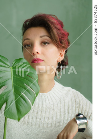 Portrait of a young beautiful woman with perfect smooth skin with a large green tropical leaf. Fashion, beauty, makeup, cosmetics, health, ecology, nature, spa, wellness. Portrait of a young beautiful woman with perfect smooth skin with a large green tropical leaf. Fashion, beauty, makeup, cosmetics, health, ecology, nature, spa, wellness. 65874528