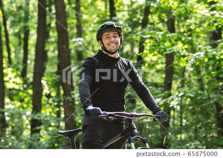 Cheerful cyclist posing with bike over forest background 65875000