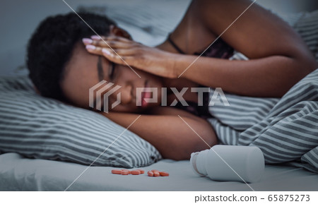Pills sprinkled from jar on bed, african american girl cannot fall asleep 65875273