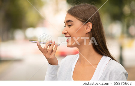 Smiling Girl Using Smartphone Voice Assistant Walking In Park Outdoors Smiling Girl Using Smartphone Voice Assistant Walking In Park Outdoors 65875662
