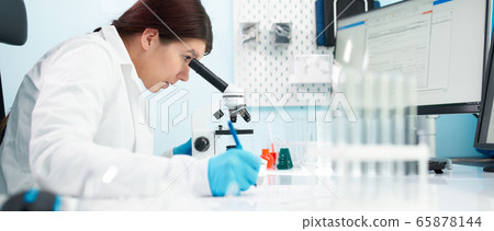 Side view of brunette lab technician looks at microscope in laboratory. Side view of brunette lab technician looks at microscope in laboratory. 65878144