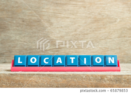 Tile letter on red rack in word location on wood background 65879853