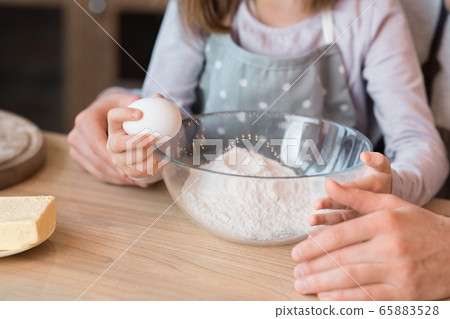 Little girl cracking egg to bowl, helping father with cooking pastry Little girl cracking egg to bowl, helping father with cooking pastry 65883528