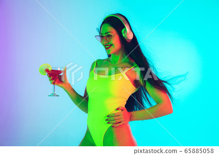 Beautiful girl in fashionable swimsuit isolated on gradient studio background in neon light. Summer, resort, fashion and weekend concept 65885058