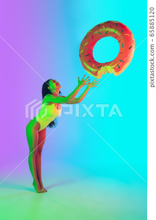 Beautiful girl in fashionable swimsuit isolated on gradient studio background in neon light. Summer, resort, fashion and weekend concept Beautiful girl in fashionable swimsuit isolated on gradient studio background in neon light. Summer, resort, fashion and weekend concept 65885120
