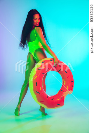 Beautiful girl in fashionable swimsuit isolated on gradient studio background in neon light. Summer, resort, fashion and weekend concept 65885136