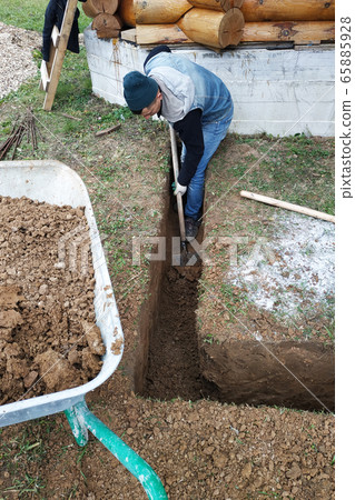 A worker digs a trench shovel near the house. A worker digs a trench shovel near the house. 65885928