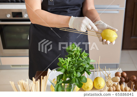 A woman forces on a lemon on a stick making a blank for her fruit bouquet 65886841