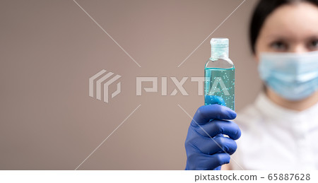 Alcohol gel to protect hands from viruses is demonstrated by a girl in a protective mask and medical peppers. 65887628