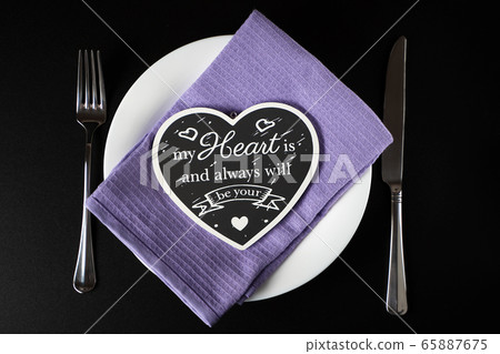 Black heart made of wood on a white plate with Cutlery on the sides 65887675