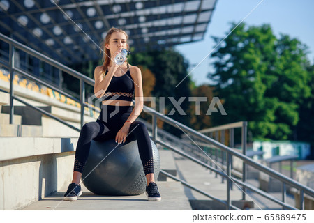 Water time. Woman leading healthy lifestyle drinking water before exercising on fitness ball Water time. Woman leading healthy lifestyle drinking water before exercising on fitness ball 65889475