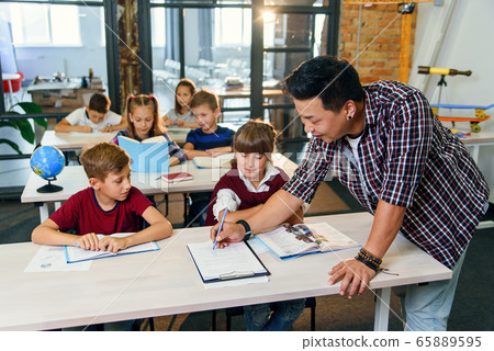 Pupils sit at desks and listens to the teacher while he explaining the topic of new lesson. 65889595