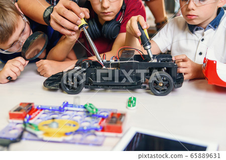 Male electronic engineer with european school children working in smart school lab and testing model of radio controlled electric car. 65889631