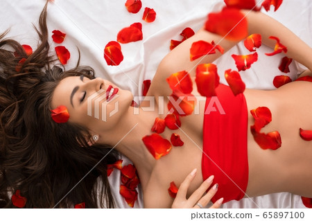 Brunette in red top on bed with flying petals high angle shot Brunette in red top on bed with flying petals high angle shot 65897100
