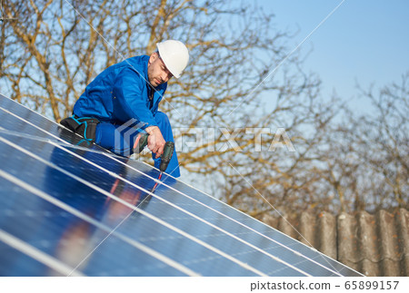 Electrician mounting solar panel on roof of modern house 65899157