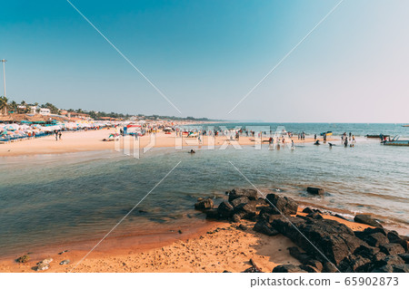 Mapusa, Anjuna, Goa, India. People Visit And Relax On Baga Beach At Sunny Evening Under Blue Sky. Mapusa, Anjuna, Goa, India. People Visit And Relax On Baga Beach At Sunny Evening Under Blue Sky. 65902873