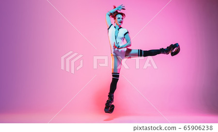 Beautiful redhead woman in a white sportswear jumping in a kangoo jumps shoes isolated on gradient studio background in neon light 65906238