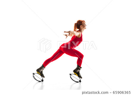 Beautiful redhead woman in a red sportswear jumping in a kangoo jumps shoes isolated on white studio background. 65906365