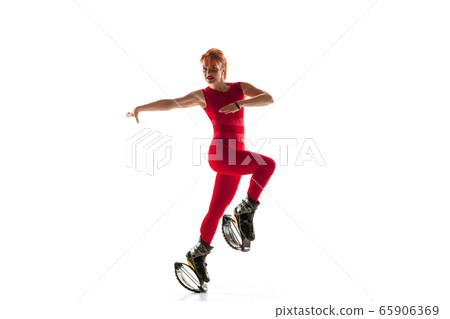 Beautiful redhead woman in a red sportswear jumping in a kangoo jumps shoes isolated on white studio background. 65906369