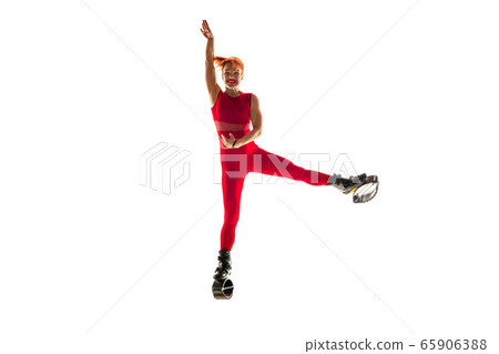 Beautiful redhead woman in a red sportswear jumping in a kangoo jumps shoes isolated on white studio background. 65906388