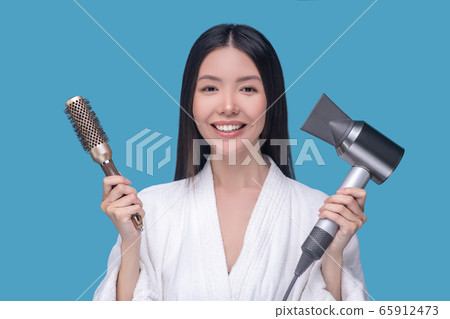 Brunette young asian woman holding a brush and a hair dryer 65912473
