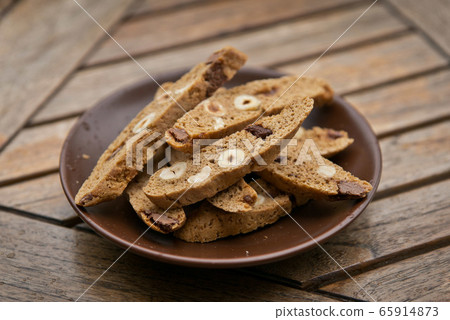 Homemade Biscotti with nuts and dark chocolate on a brown plate on a wooden table 65914873