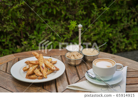a plate of homemade biscotti cookies and a Cup of coffee with cream and sugar on the wooden table. Blurred background 65914915