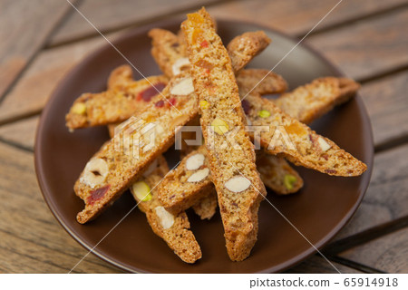 homemade Biscotti with nuts and candied fruits on a brown plate on a wooden table homemade Biscotti with nuts and candied fruits on a brown plate on a wooden table 65914918