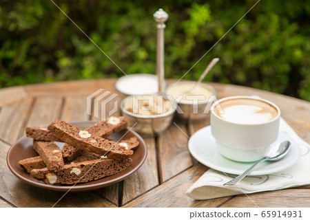 A plate of homemade chocolate biscotti and a Cup of coffee with cream and sugar on the wooden table. Blured backgroung 65914931