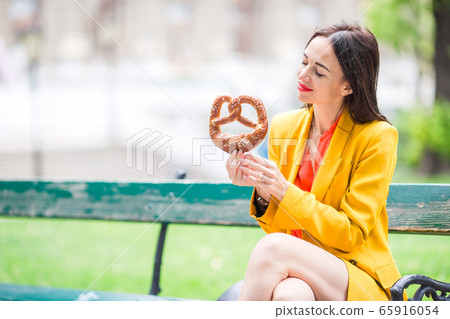 Beautiful young woman holding pretzel and relaxing in park 65916054