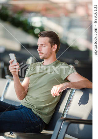 Passenger in a airport lounge waiting for flight aircraft. Young man with cellphone in airport waiting for landing Passenger in a airport lounge waiting for flight aircraft. Young man with cellphone in airport waiting for landing 65916133