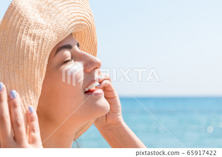 Smiling woman in hat is applying sunscreen on her Smiling woman in hat is applying sunscreen on her 65917422