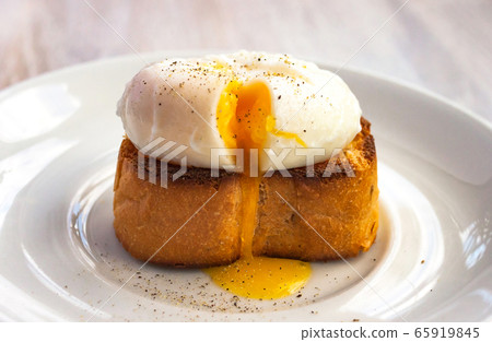 Poached egg, liquid yolk with, green onion on toast bread, white plate on white wooden background Poached egg, liquid yolk with, green onion on toast bread, white plate on white wooden background 65919845