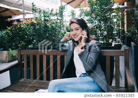 Smiling female talking on smartphone on bench Smiling female talking on smartphone on bench 65921385