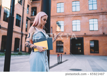 Focused woman with notebooks using smartphone on street Focused woman with notebooks using smartphone on street 65921487