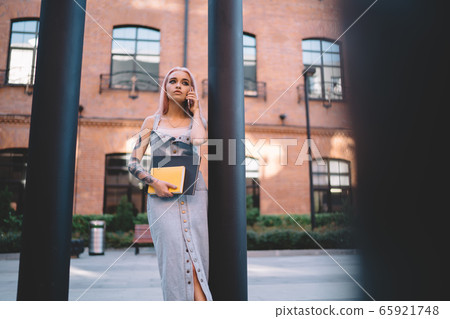 Serious female speaking on smartphone near column Serious female speaking on smartphone near column 65921748
