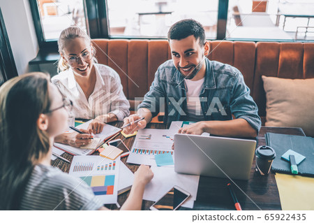 Smiling freelancers discussing charts in cafe. Colleagues collaborating Smiling freelancers discussing charts in cafe. Colleagues collaborating 65922435